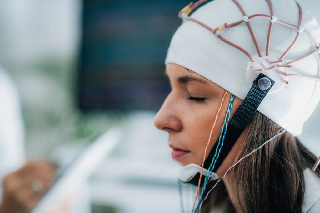 A person wearing a white cap with electrodes attached, possibly for a brain activity study, with their eyes closed.